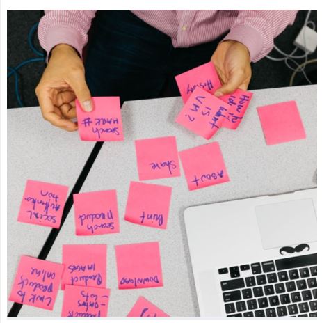 Hands sorting pink sticky notes next to keyboard